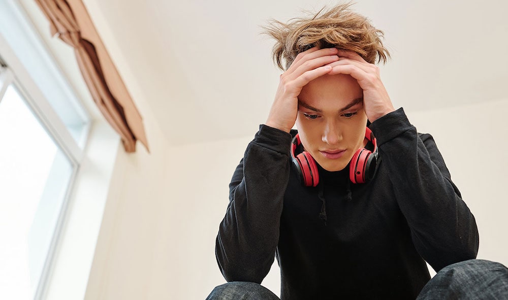 teen boy wearing headphones around neck looking down with head in hands