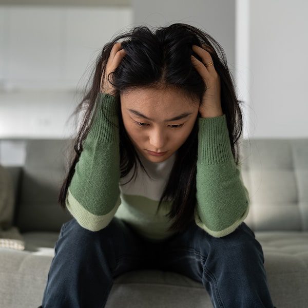Care concepts therapy young girl sitting on sofa with head in hands-min young girl sitting on sofa with head in hands