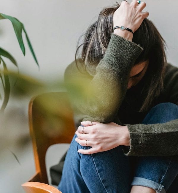 woman sitting on chair with knees to chest and head down